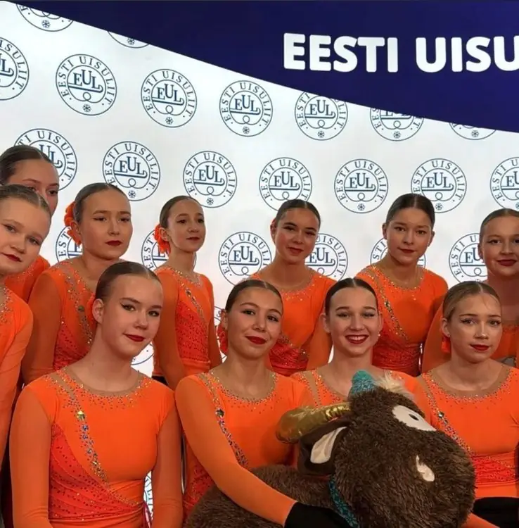 Rühmauisutamise võistkond oranžides kostüümides Eesti Uisuliidu taustal