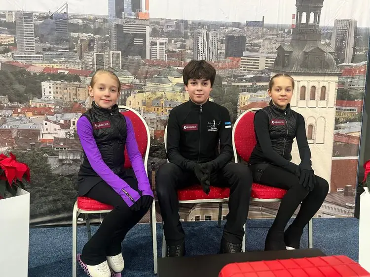 Kolm noort uisutajat istumas võistlusel Tallinna panoraami taustal