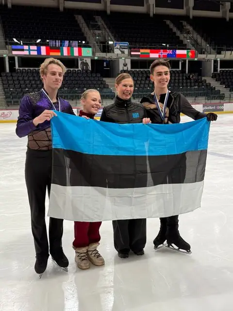 Medalitega uisutajad ja treener Eesti lipuga jäähallis