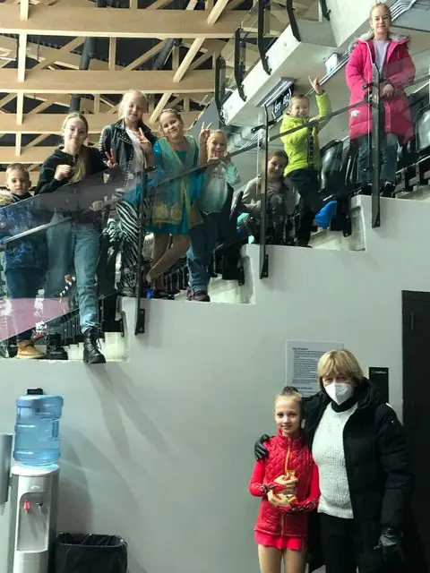 Lapsed lehvitavad jäähalli tribüünil, all uisutaja koos treeneriga