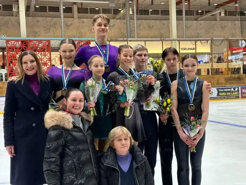Medalite ja lilledega noored uisutajad koos treeneritega jääl
