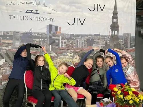 Rõõmsad noored uisutajad poseerimas Tallinn Trophy võistluse taustaseina ees