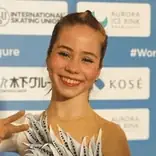 A smiling woman in a white leotard, possibly a figure skater, in front of a blue and white backdrop